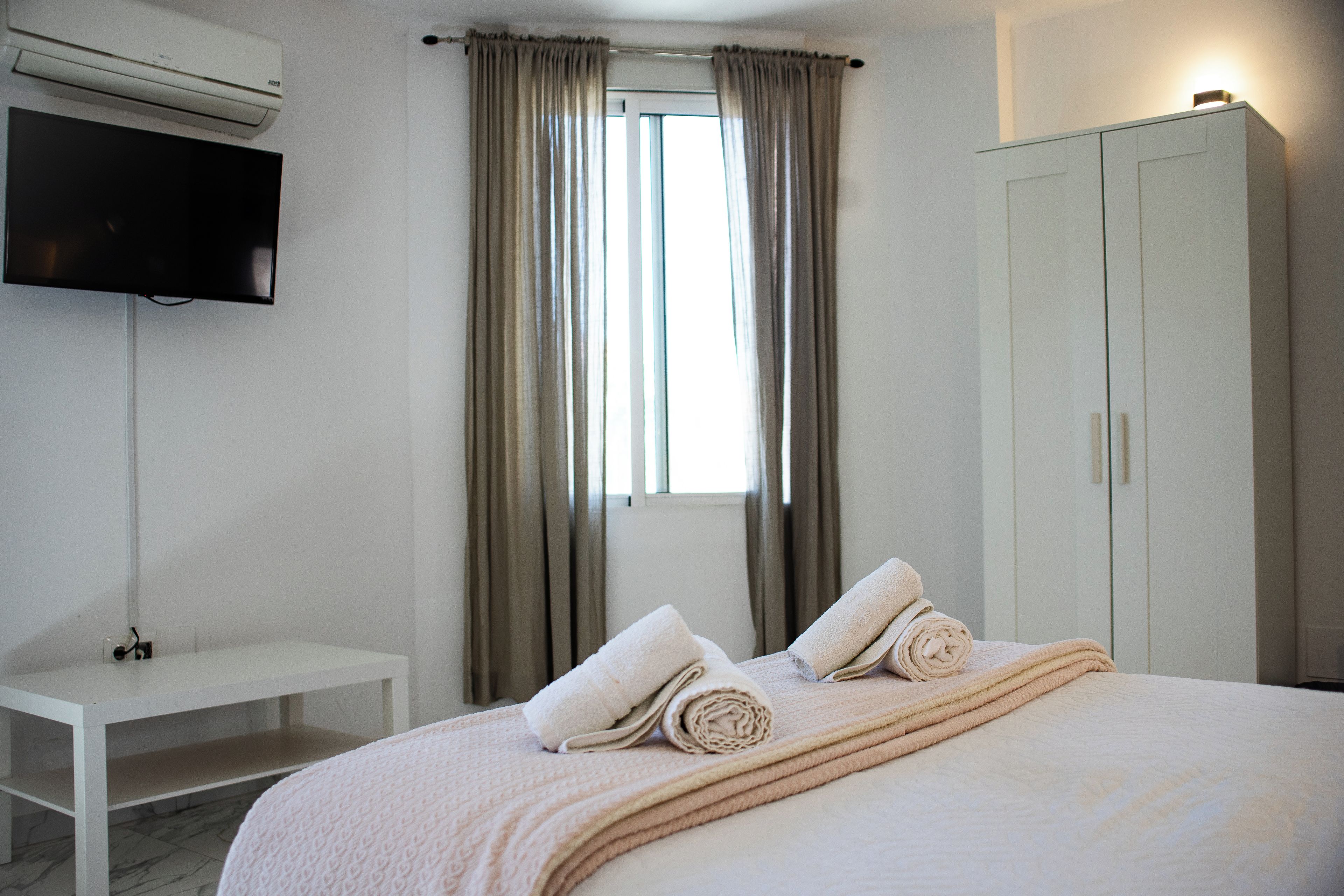 Habitación de hotel con cama, televisor montado en la pared, armario y ventana con cortinas.