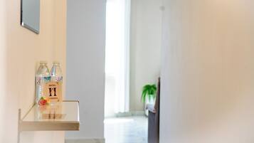 Ein Hotel-Empfangsbereich mit freier Sicht auf den zur Zimmerflur führenden Gang. Auf einem Regal stehen zwei Wasserflaschen, und in der Ferne ist ein Blumentopf zu sehen.