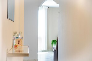 En hotellreception med fri sikt över korridoren som leder till ett rum. På en hylla står två vattenflaskor, och längre bort syns en krukväxt.