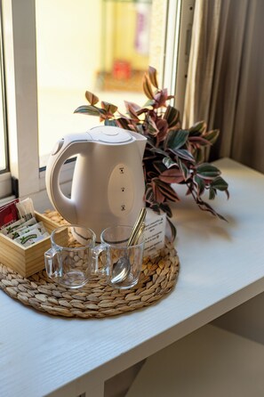Une bouilloire électrique blanche posée sur un set de table en fibres tressées, une tasse en verre, une cuillère et une boîte de sachets de thé, le tout sur un rebord de fenêtre.
