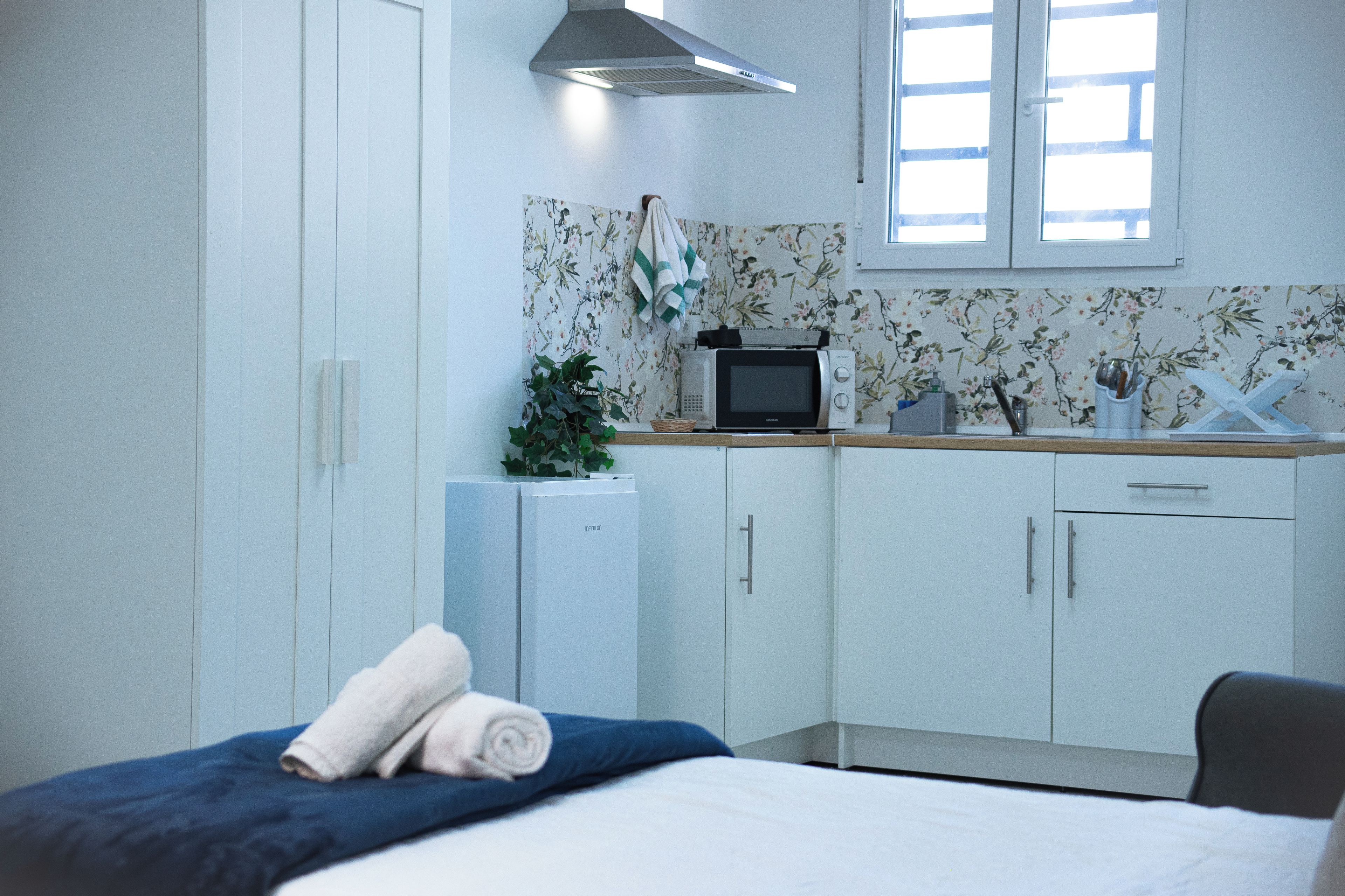 A hotel room with a bed, a small kitchenette, and a window.