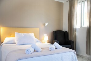 A hotel room with a bed, pillows, a chair, a lamp, and a window with curtains. - Hotel Avenida (Velez-Malaga)