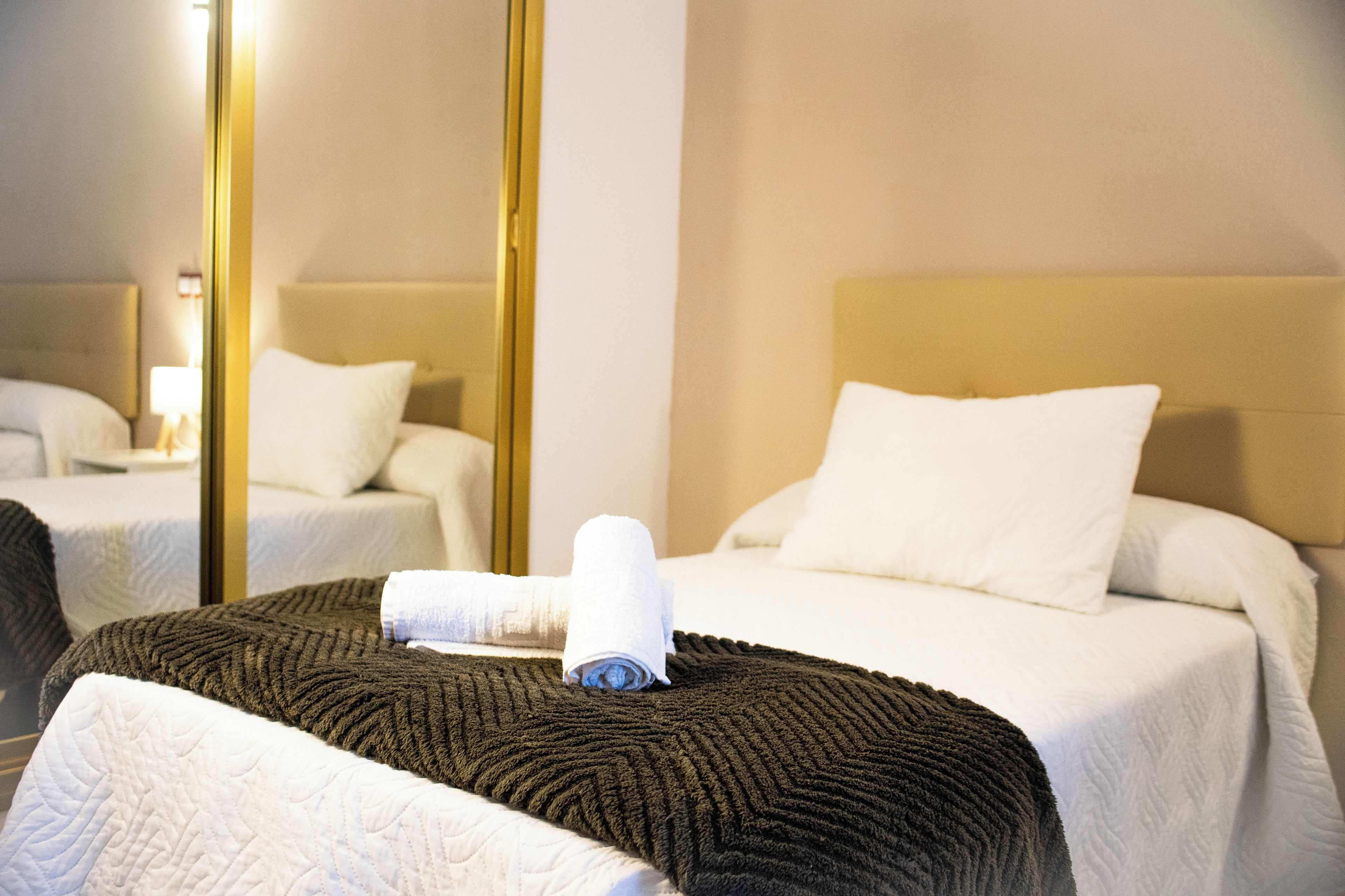 A hotel room with a bed, a bedside table, a mirror, and a window.