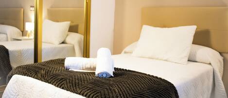 A hotel room with a bed, a bedside table, a mirror, and a window.