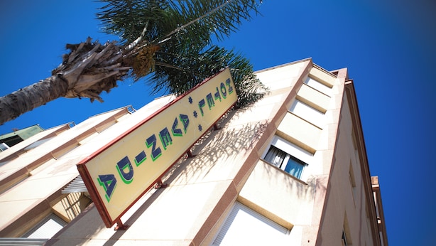 A building with a signboard, windows, and a palm tree. - Hotel Avenida (Velez-Malaga)