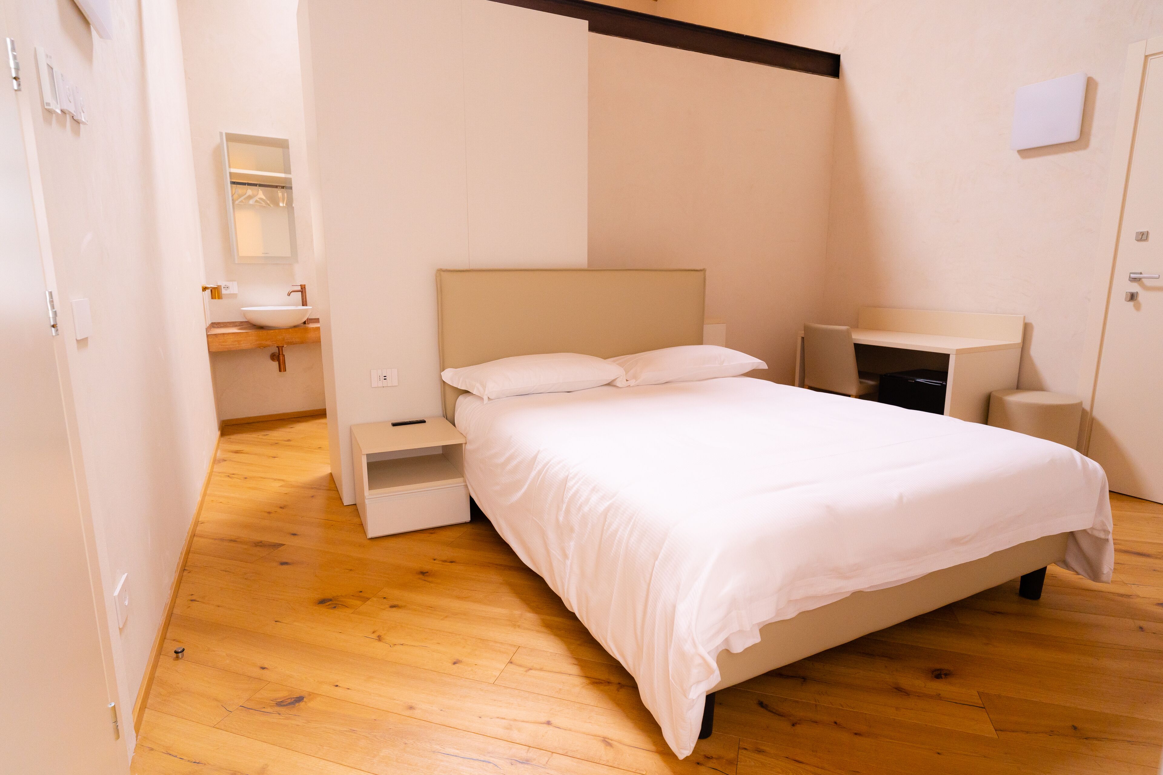 A bedroom with a bed, bedside tables, a built-in bench, a mirror, and a bathroom with a sink and towel rack.