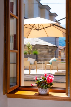 A window with a view of an outdoor patio area, including a table and chairs, and a potted plant with flowers. - Locanda Alberti (Mandello del Lario)