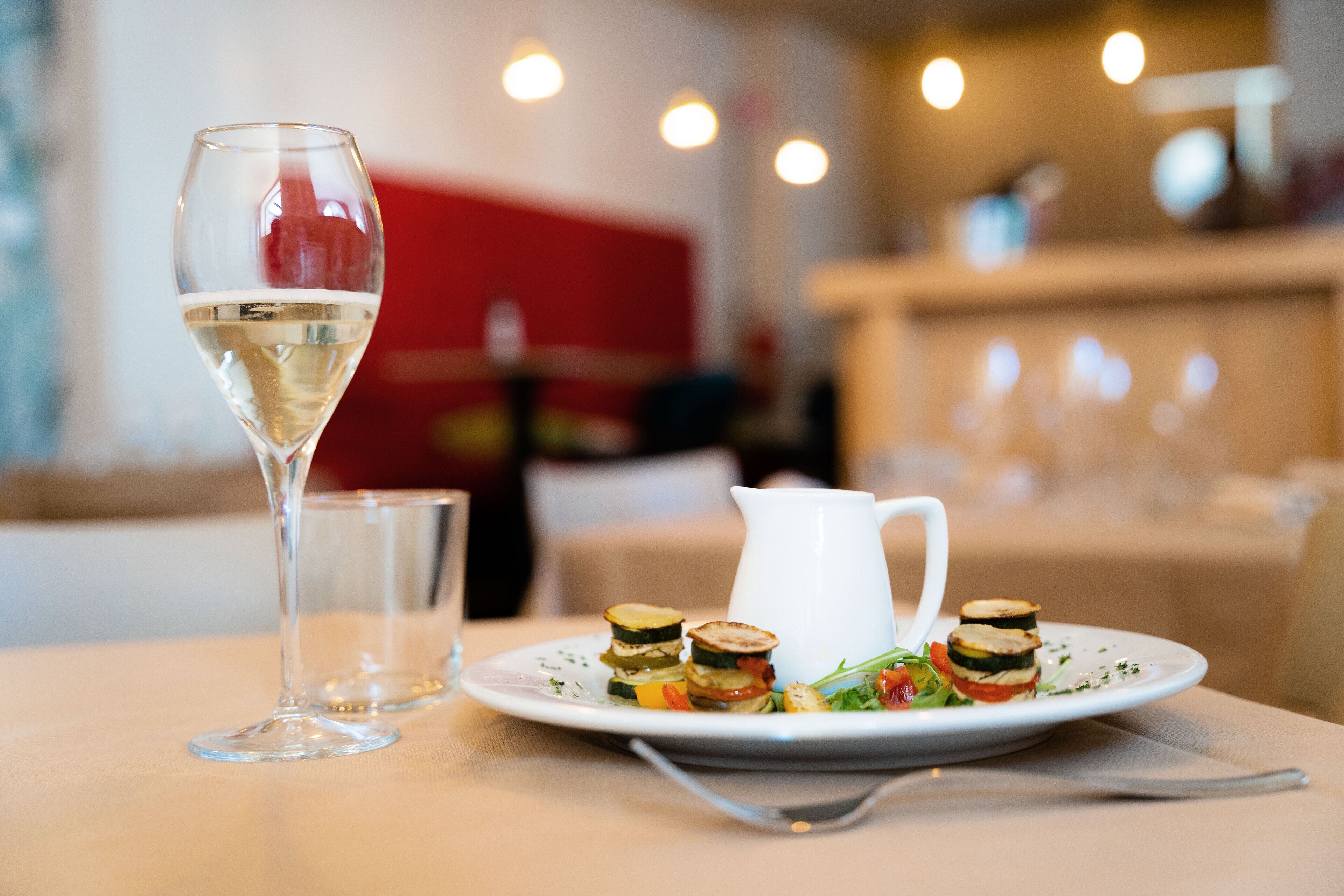 Een eettafel met een schotel groenteterrices, een glas witte wijn en een witte karaf.