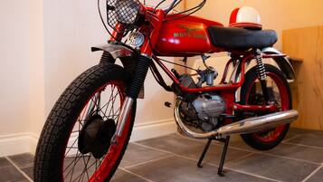 Una motocicleta antigua con una combinación de colores rojo y negro, una canasta en la parte delantera y un asiento cubierto de negro.