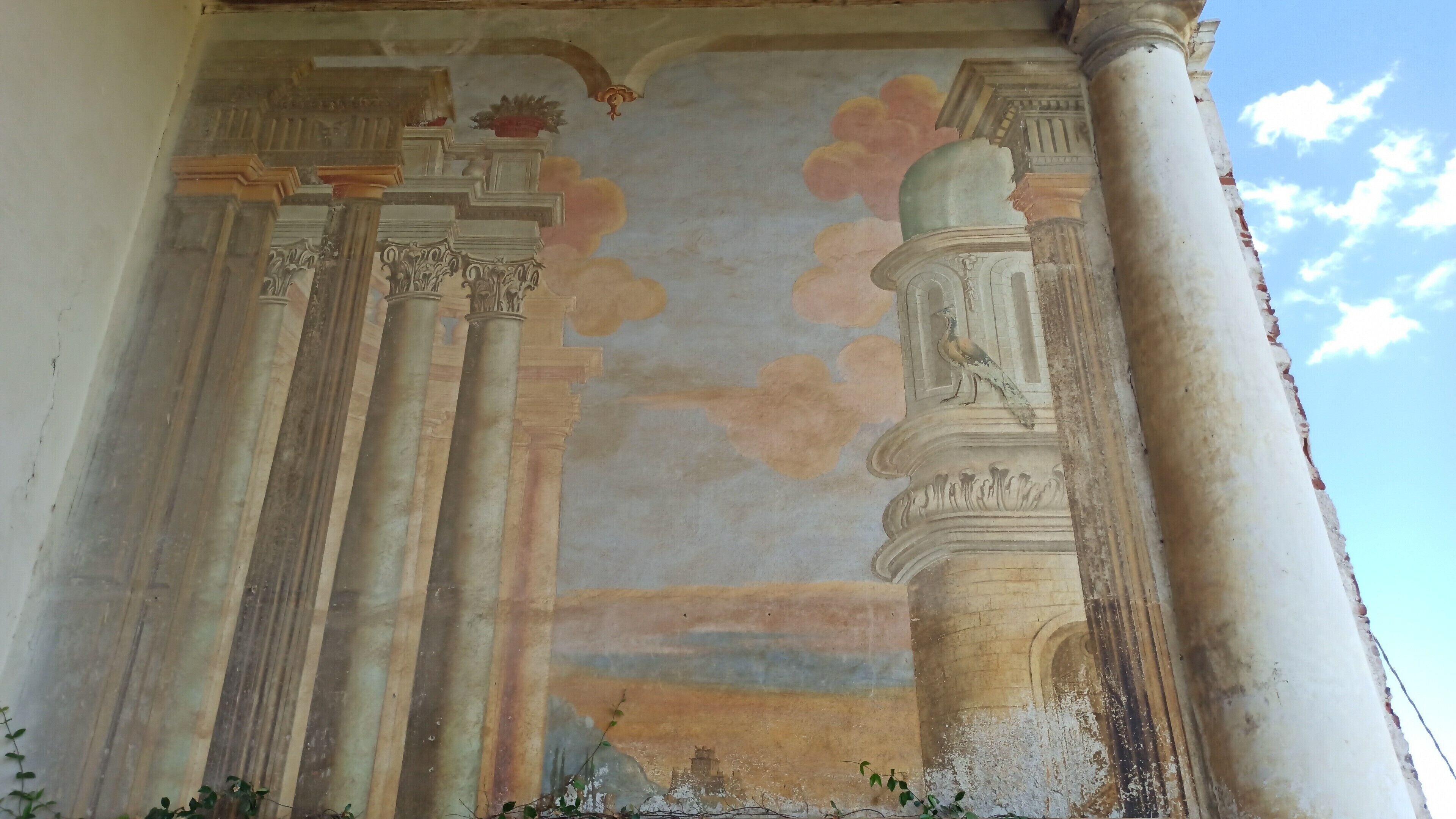 A classical architectural structure with columns and a painted sky mural.