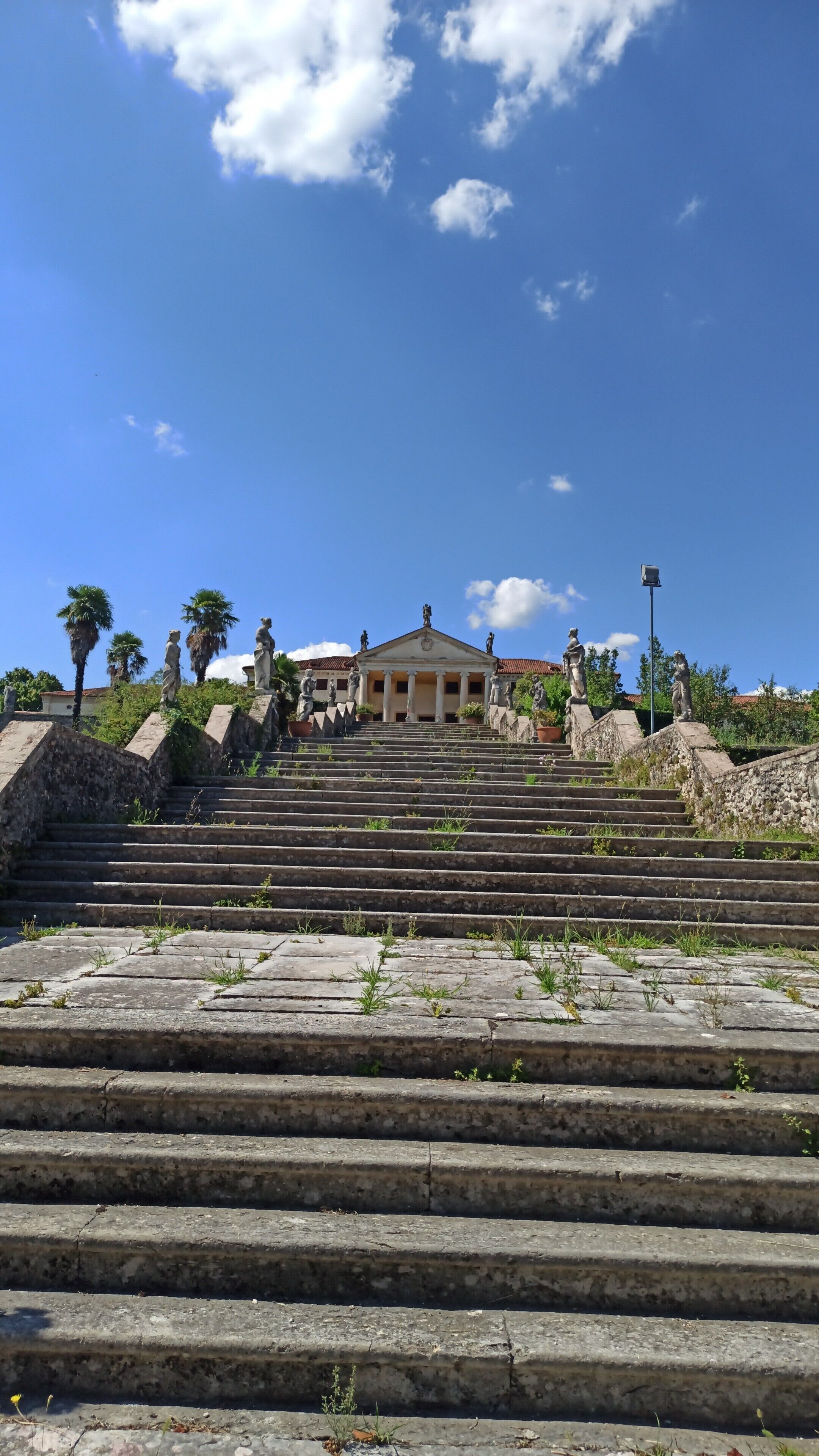 Eine Treppe aus Stein führt zu einem klassizistischen Gebäude mit Säulen und Statuen.
