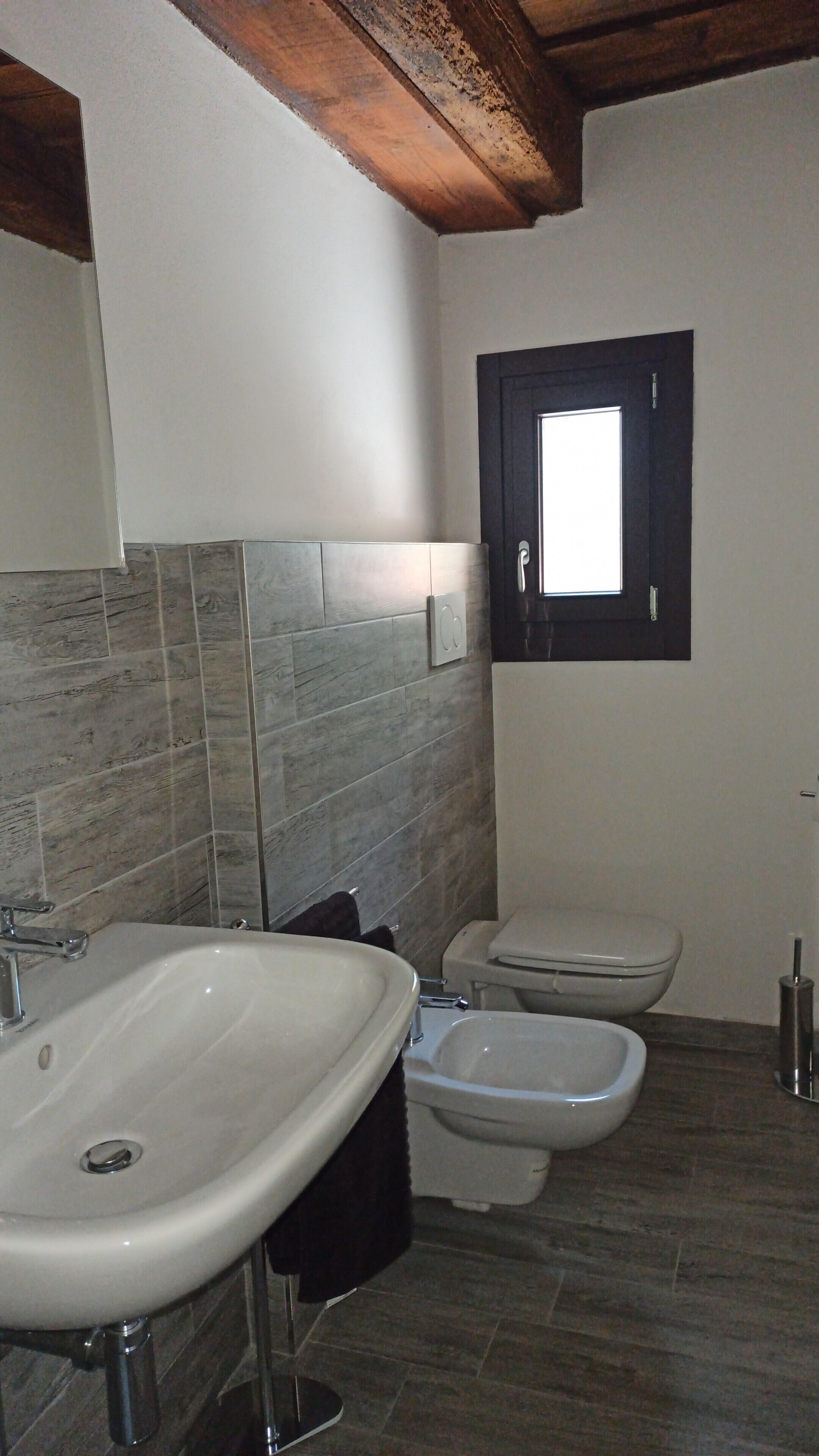 A bathroom with a white sink, a toilet, and a bidet. The walls are tiled, and there is a window above the toilet.