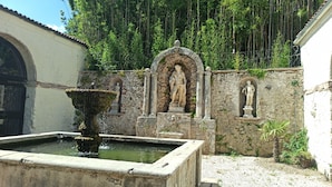 Une cour avec une fontaine, des statues en pierre et un mur couvert de végétation.