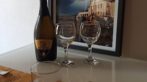 Une table avec une bouteille de vin, deux verres à vin, une assiette et des couverts. Un tableau représentant un bâtiment et un ciel nuageux est accroché au mur derrière.