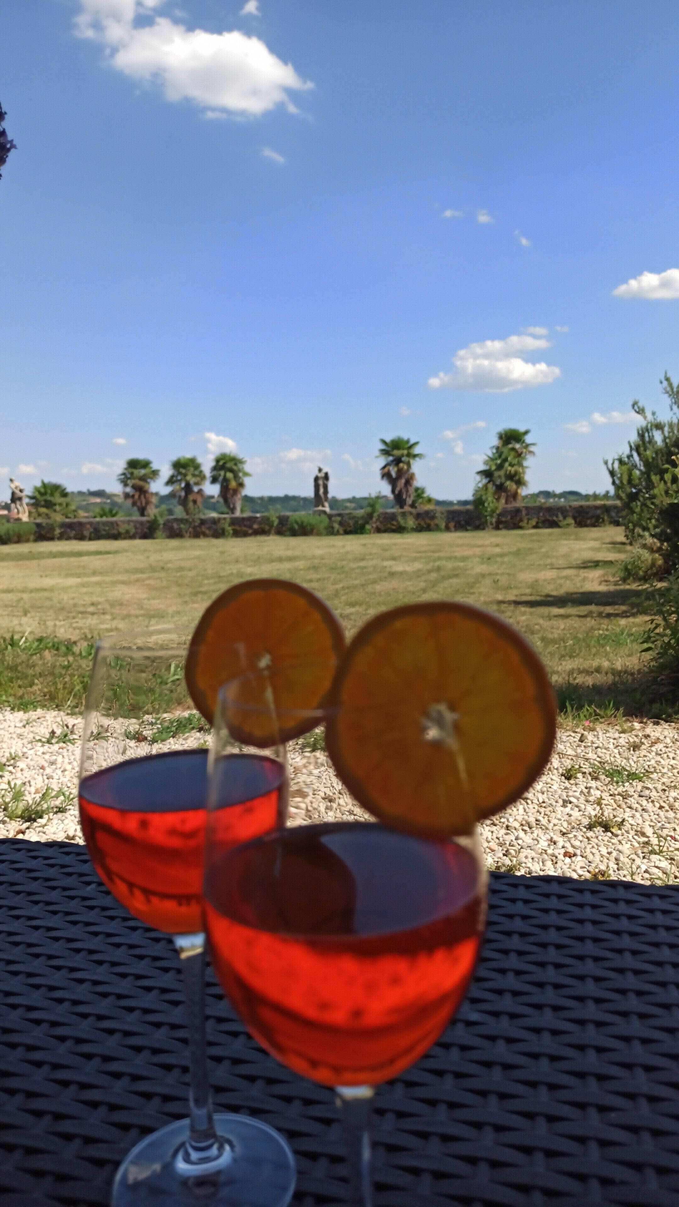Two glasses of red beverage with a tropical fruit garnish on a table outdoors.