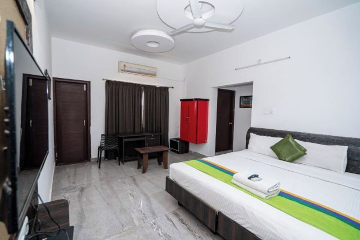 A hotel room with a bed, a desk, a chair, a TV, and a red wardrobe.