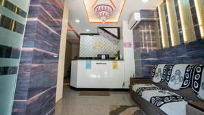 A reception area with a modern design, including a reception desk, a sofa with patterned cushions, and a decorative ceiling light.