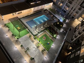 Eine Luftaufnahme eines modernen Innenhofs eines Hotels, mit Swimmingpool, Außenmöbeln und viel Grün.
