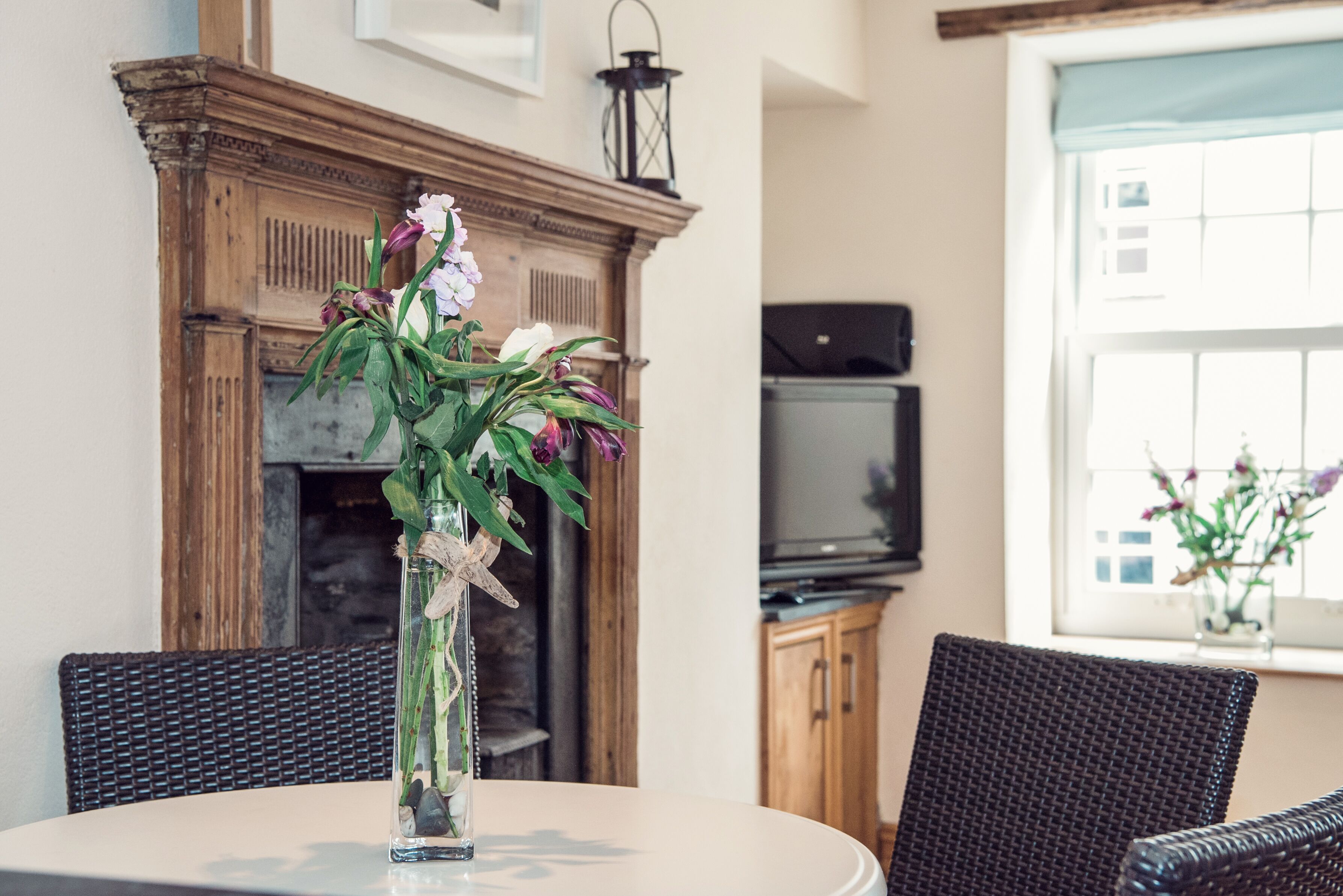 A dining area with a round table, wicker chairs, a fireplace, and a television.