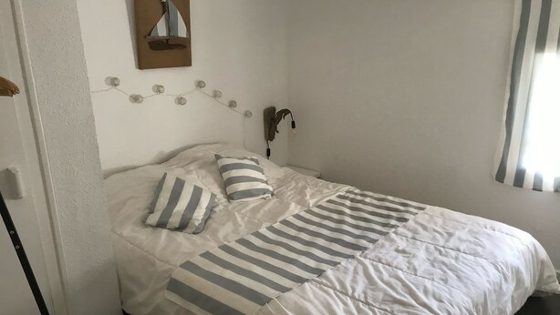 A neatly made bed with striped bedding, a wall-mounted mirror, and a string of lights. - Seasonal rental (Les Mathes)
