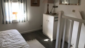 A bedroom with a bed, a dresser, a lamp, a mirror, and a window with curtains. - Seasonal rental (Les Mathes)