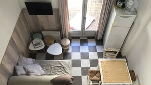 A compact room with a checkered floor, a sofa, a small table, and a fan. - Seasonal rental (Les Mathes)