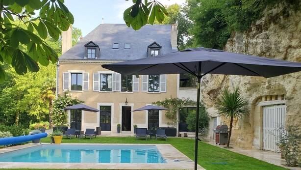A backyard with a swimming pool, outdoor seating, and a large house with multiple windows and shutters. - Domaine du Val Sauvage (Langeais)