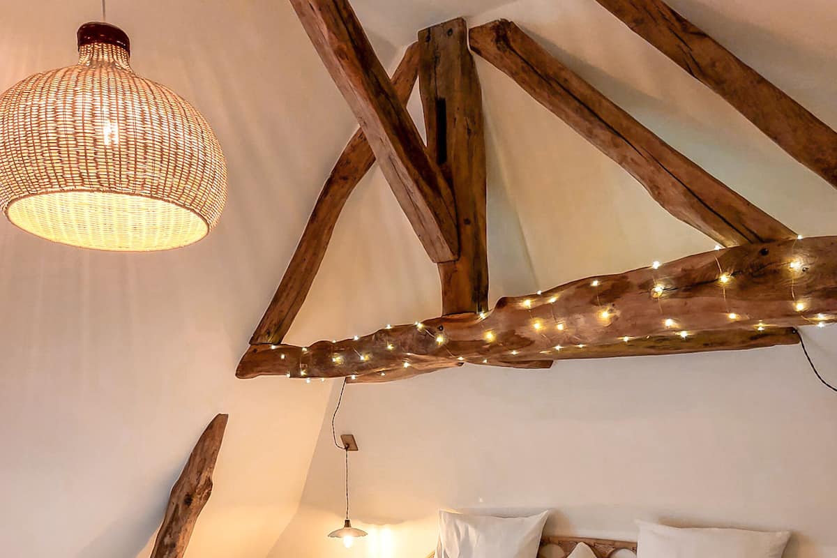 Un dormitorio con una cama, almohadas, una lámpara colgante y vigas de madera.