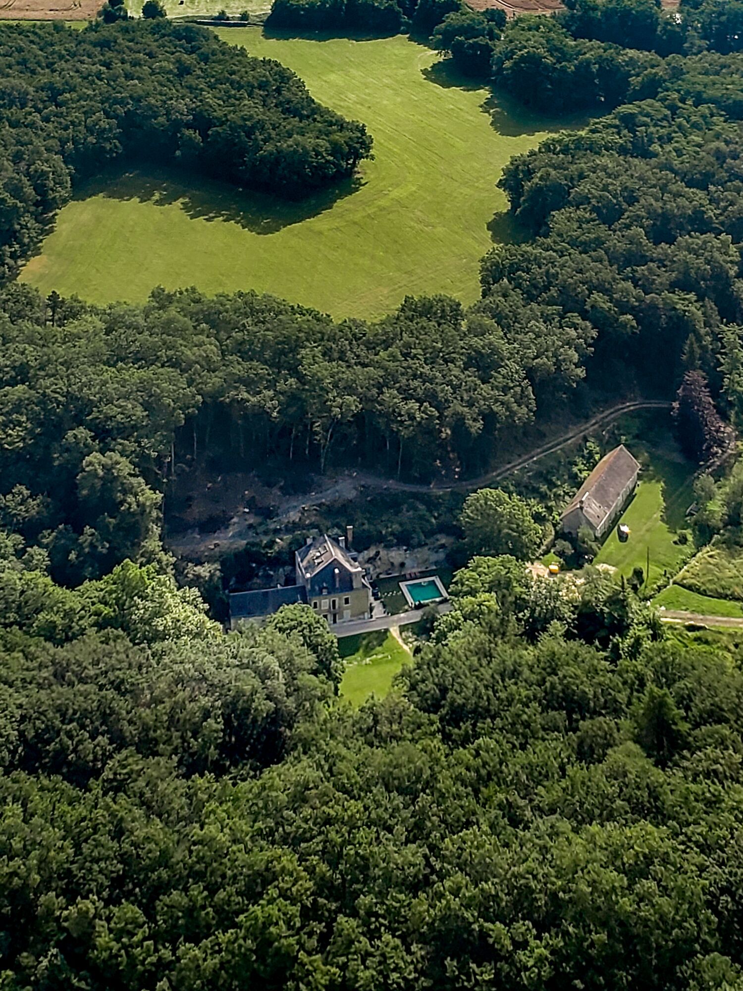 An aerial view of a large estate with a main house, a swimming pool, and extensive green lawns.