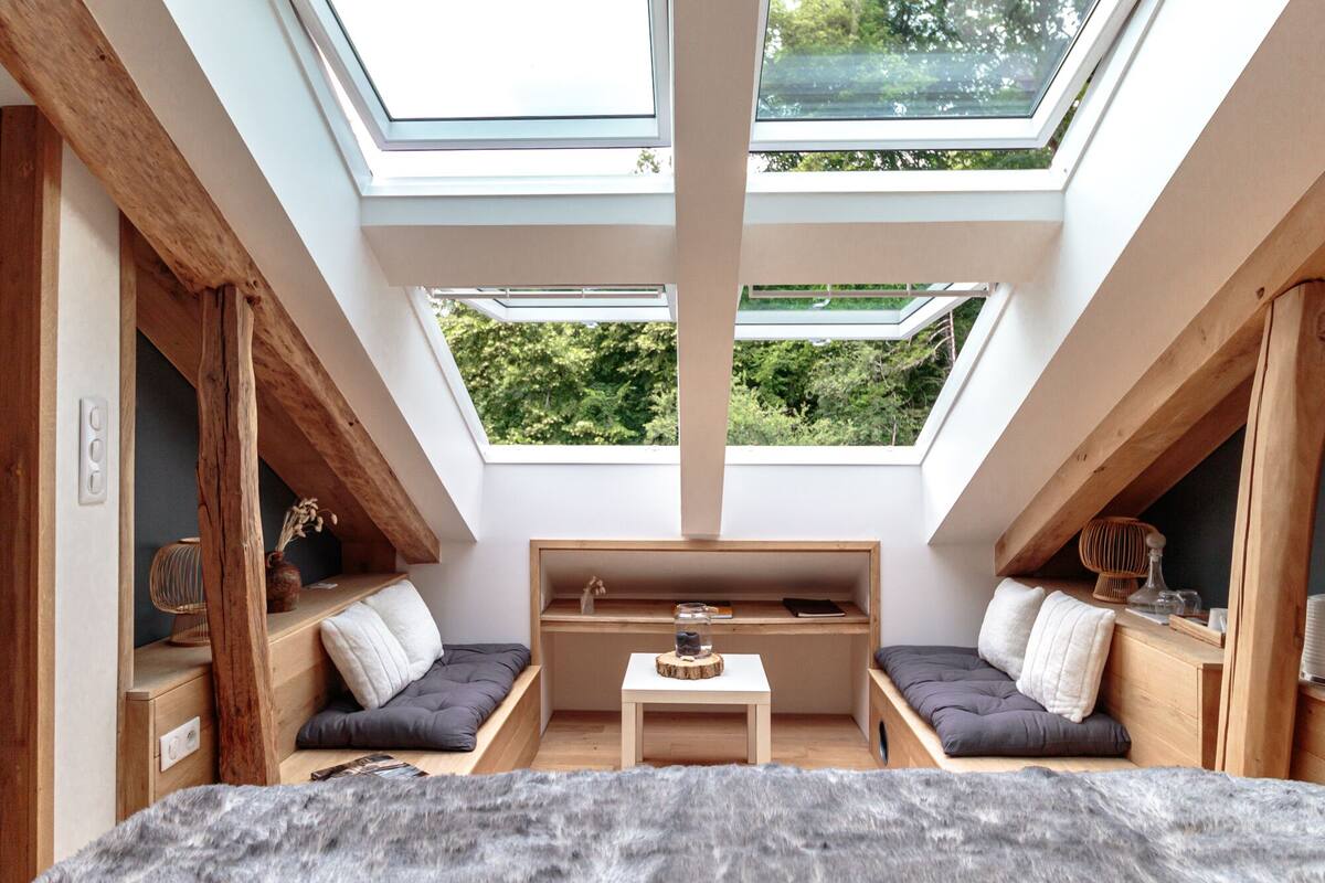 Una habitación acogedora con techo inclinado, tragaluces, una cama, dos zonas de descanso y una mesita.