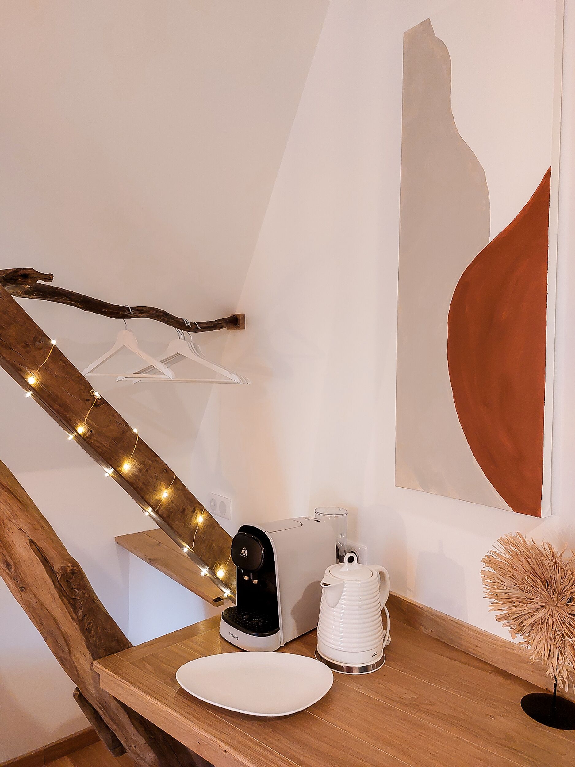A wooden dining table with a coffee maker, a glass, and a white plate.