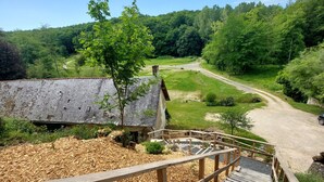 A wooden staircase leading to a building with a sloped roof, surrounded by a forested area and a dirt path. - Domaine du Val Sauvage (Langeais)