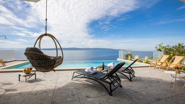 A poolside area with a hanging chair, lounge chairs, and a view of the sea.
