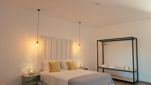 Un dormitorio con cama, lámparas de noche, mesita de noche, un espejo grande y un estante con toallas.