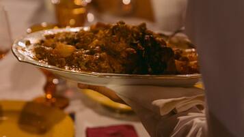 A person serving a dish on a tray at a dining table with a red napkin and a spoon.