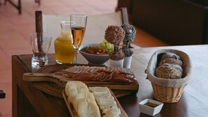Una mesa de madera con diversos alimentos, como pan, queso y una botella de jugo, ubicada en un comedor con sillas y vistas al exterior.