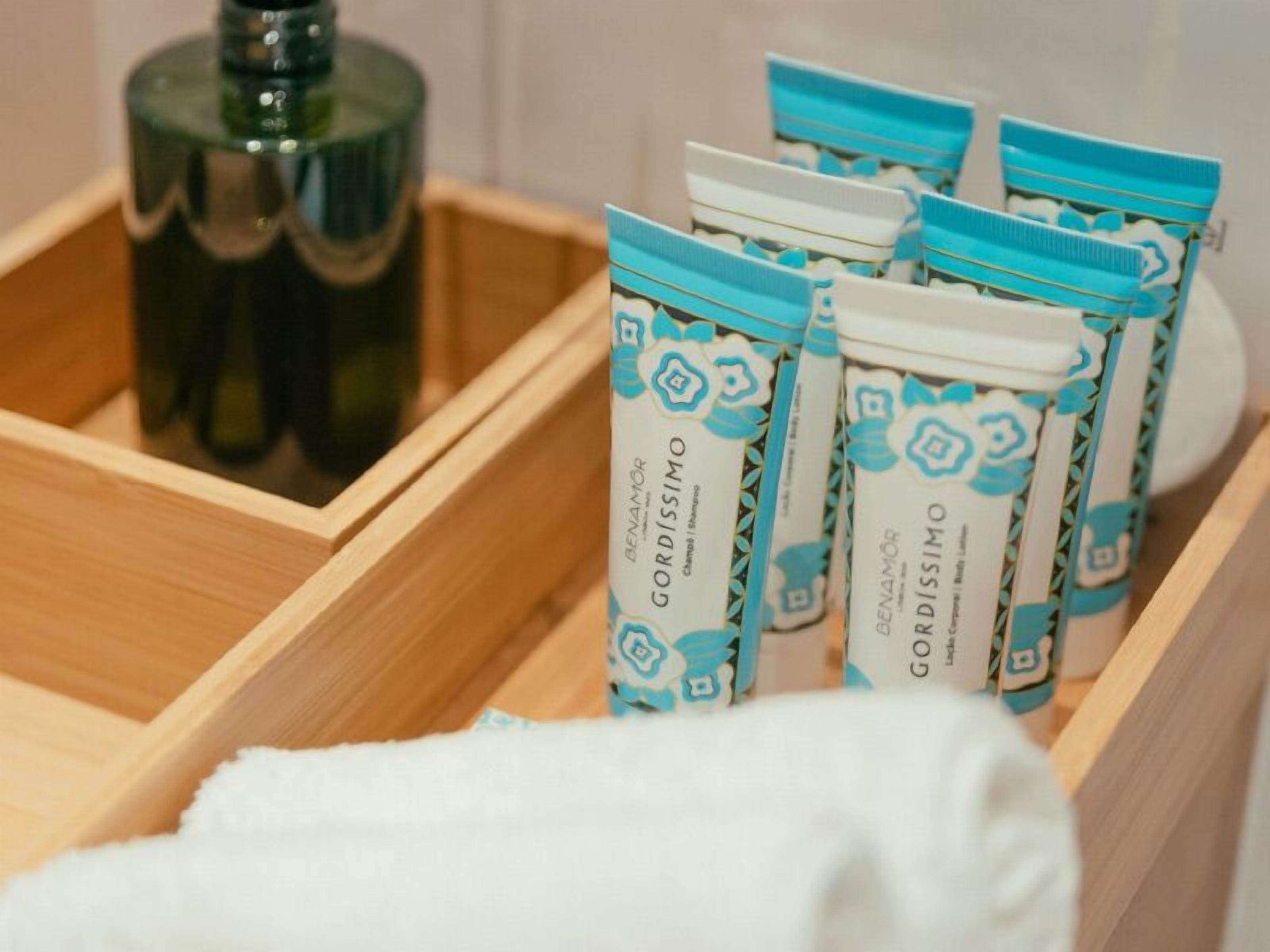 Un vassoio di legno con diversi articoli da toilette, tra cui una bottiglia e confezioni monouso.