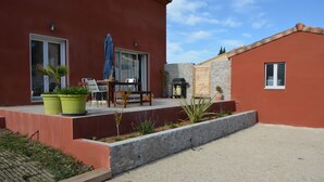 Un edificio rojo con un patio, una mesa con sillas y una parrilla.