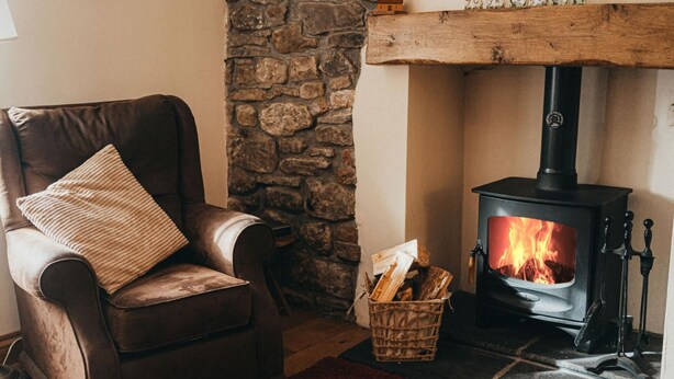 A cozy room with a stone wall, a brown leather armchair with a cushion, a red rug, and a wood-burning stove. - Cottage - Sleeps 4 - Garden - Parking (Llanelli)