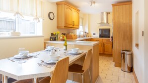 A modern kitchen with wooden cabinets, a dining table set for four, and a stainless steel sink. - Cottage - Sleeps 4 - Garden - Parking (Llanelli)