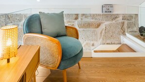 Ein gemütliches Wohnzimmer mit einem blaugrünen Sofa, Korbstühlen, einem Holztisch und einer Steinwand.