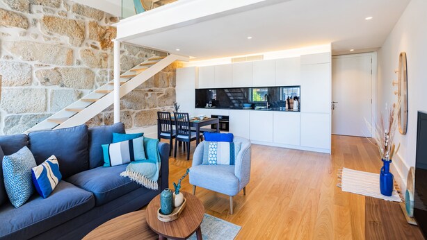 Ein moderner Wohnraum mit Steinwand, einer Treppe, einer Küche und einer Sitzecke mit Sofa und Sesseln.