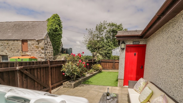 A backyard with a hot tub, a red door, and a small garden. - Bwthyn Pengwern (Caernarfon)