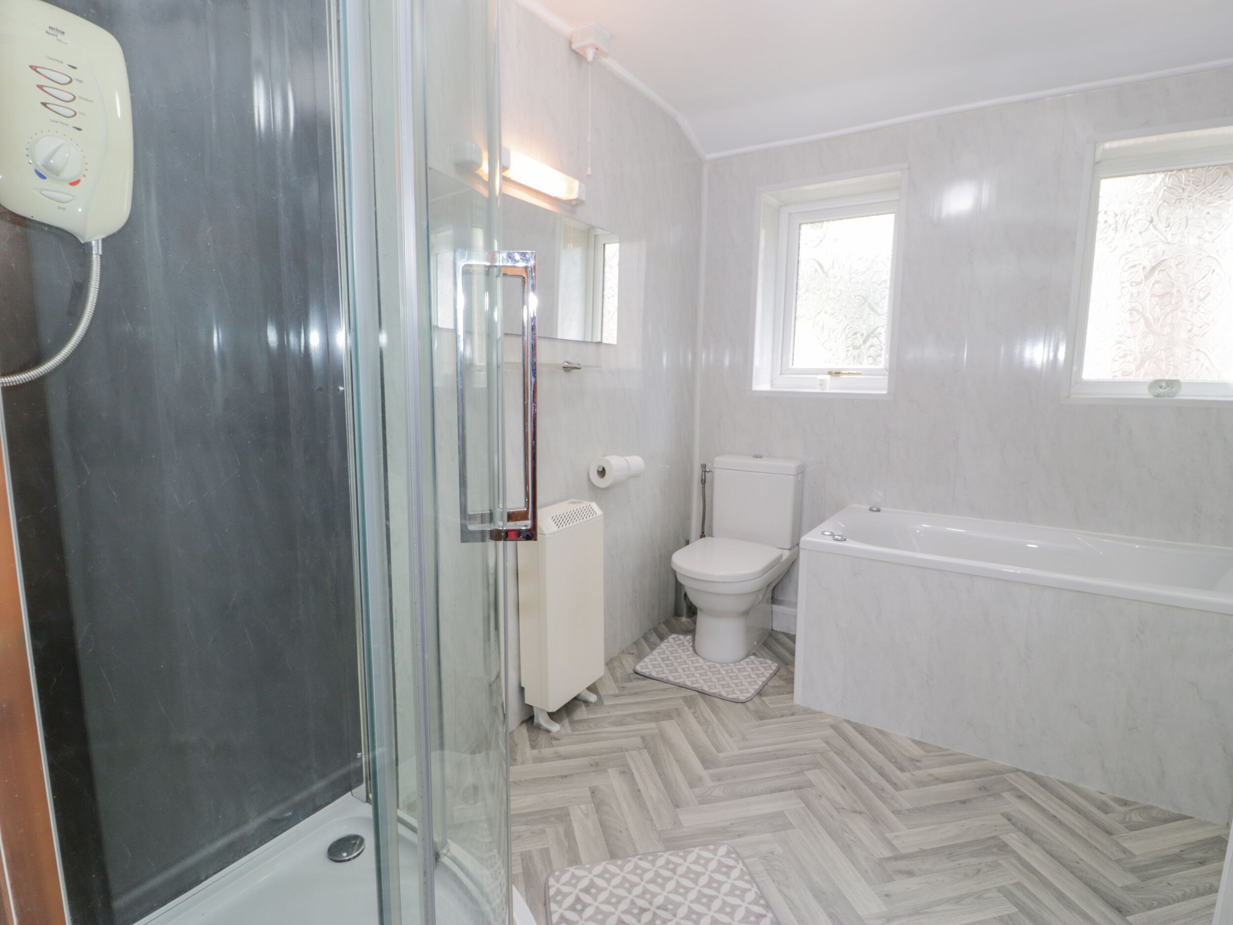 A modern bathroom with a glass shower enclosure, a toilet, a bathtub, and a window.