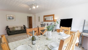 A dining area with a table set for six, surrounded by wooden chairs. There is a sofa and a fireplace in the background. - Bwthyn Pengwern (Caernarfon)