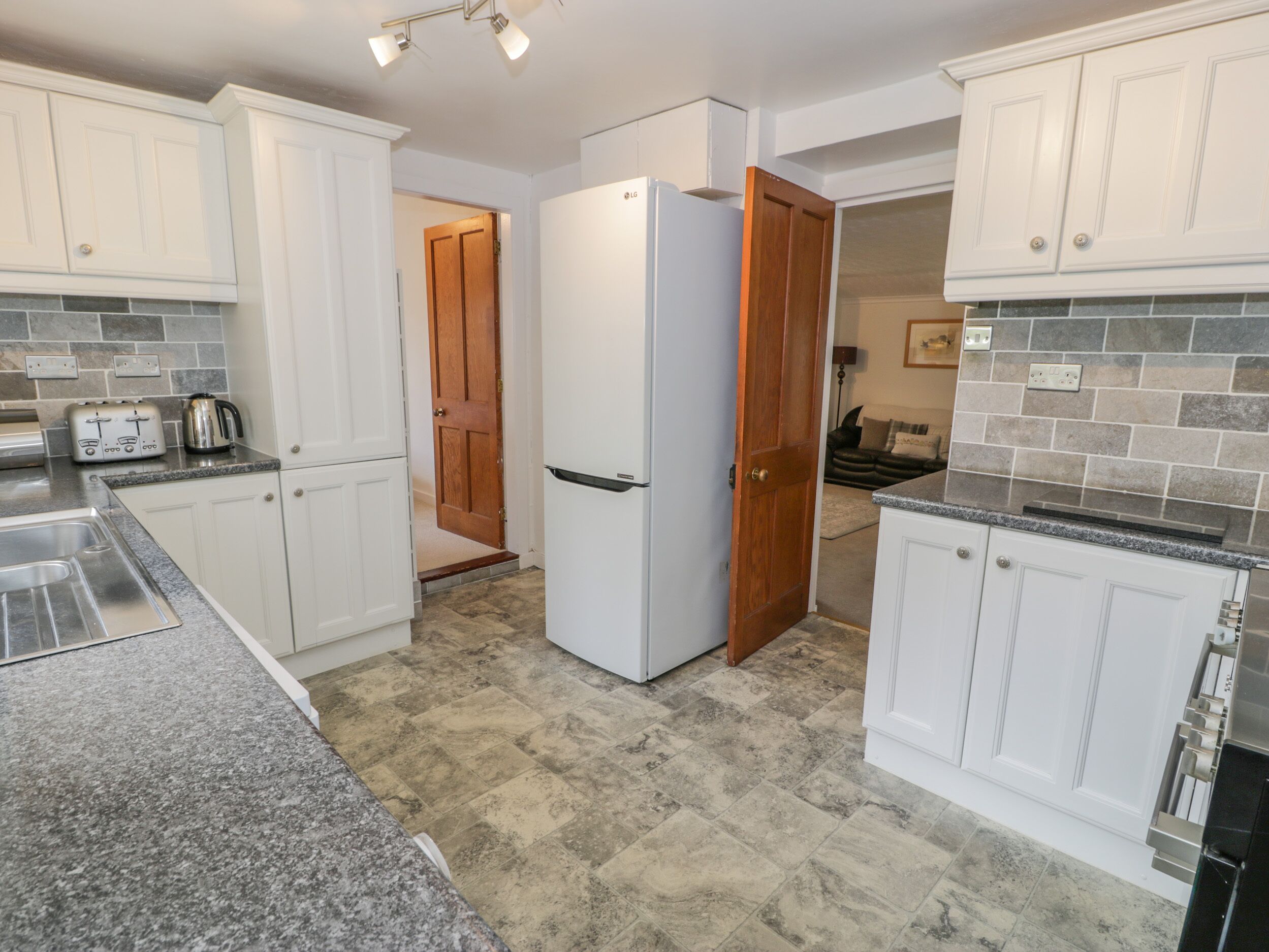 A kitchen with white cabinets, a white refrigerator, granite countertops, and a tiled floor.