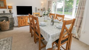 A dining room with a table set for six, a fireplace, a television, and a window with curtains. - Bwthyn Pengwern (Caernarfon)
