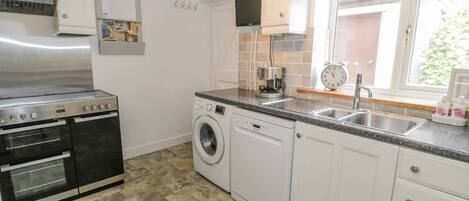 A kitchen with white cabinets, a stainless steel range, a washing machine, and a sink.