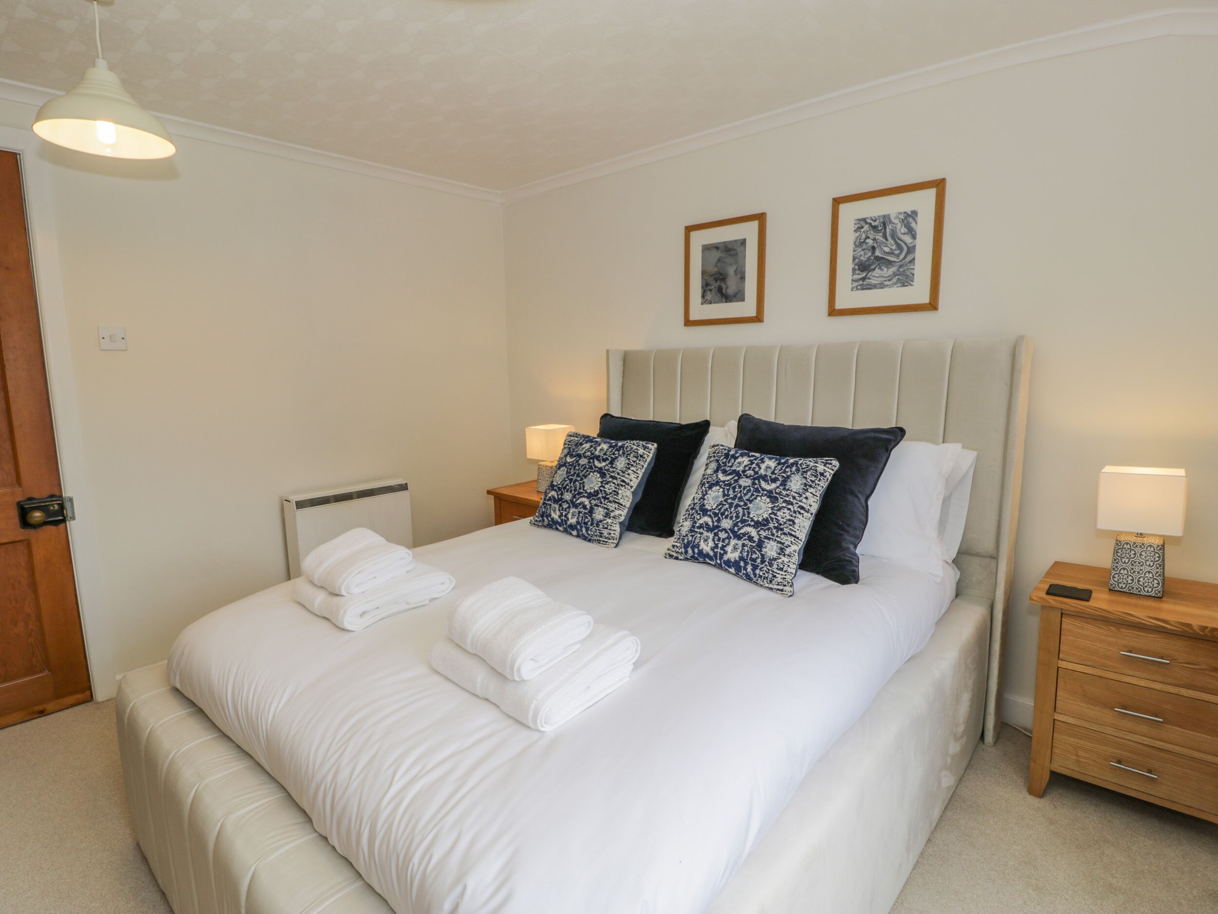 A neatly made bed with white linens and decorative pillows, a bedside lamp, and a framed artwork on the wall.