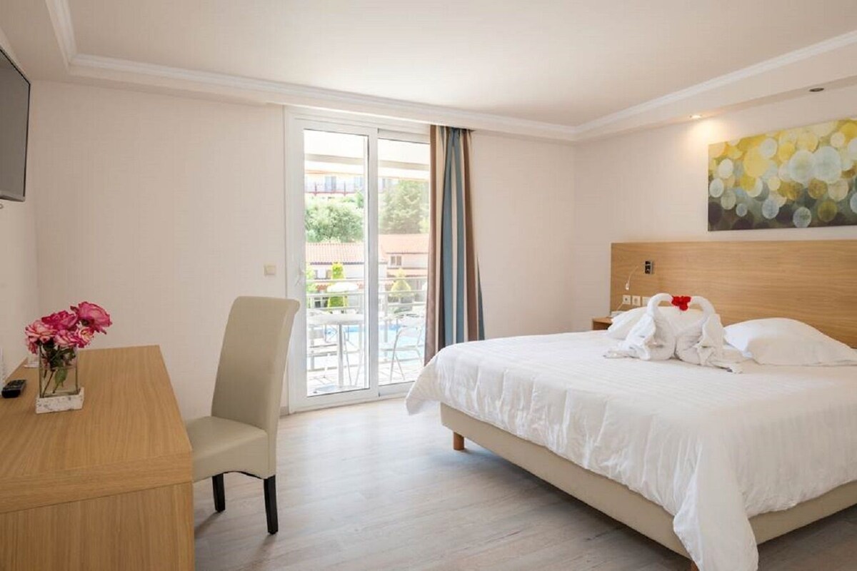 Ett hotellrum med en säng, ett skrivbord, en stol, en tavla och utsikt över omgivningarna.
